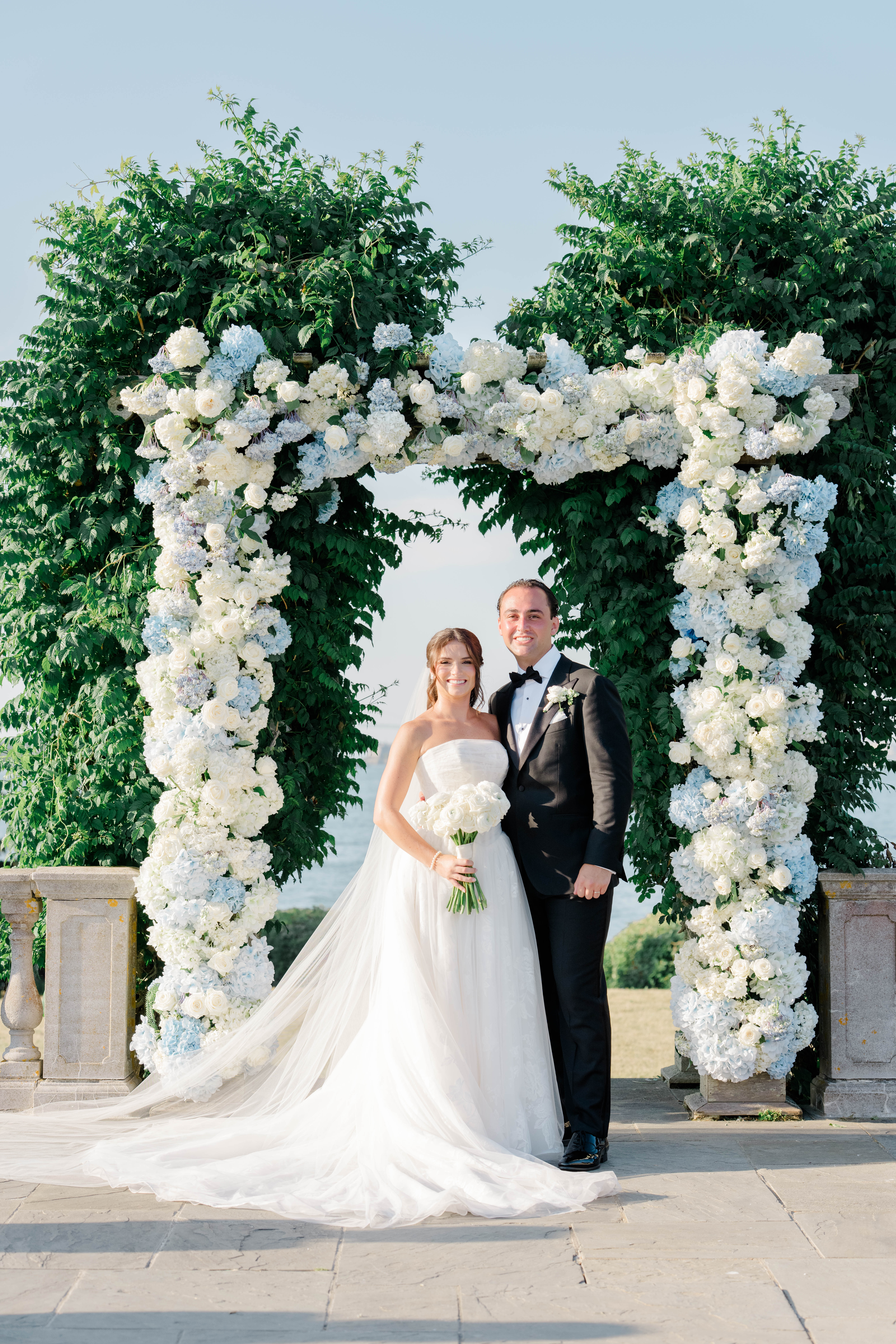 New England Wedding Photographer captures bride and groom at lovely Newport, RI wedding in front of flower-filled arch.
