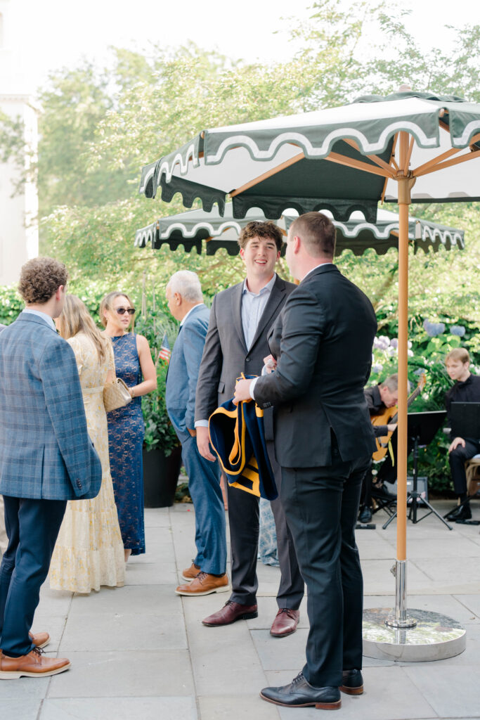 Wedding guests mingle beneath striped umbrellas during an outdoor cocktail hour, capturing the relaxed pace of a New England destination wedding.