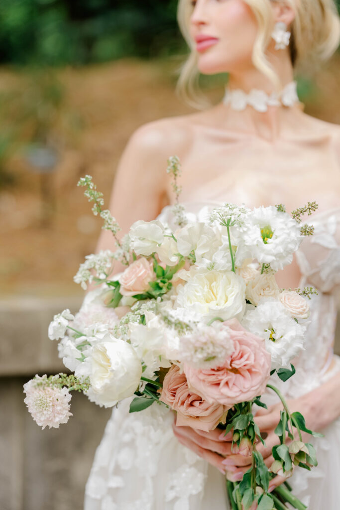 Close portrait of a bride holding a blush-and-white floral bouquet with soft garden blooms, styled for a refined New England wedding.
