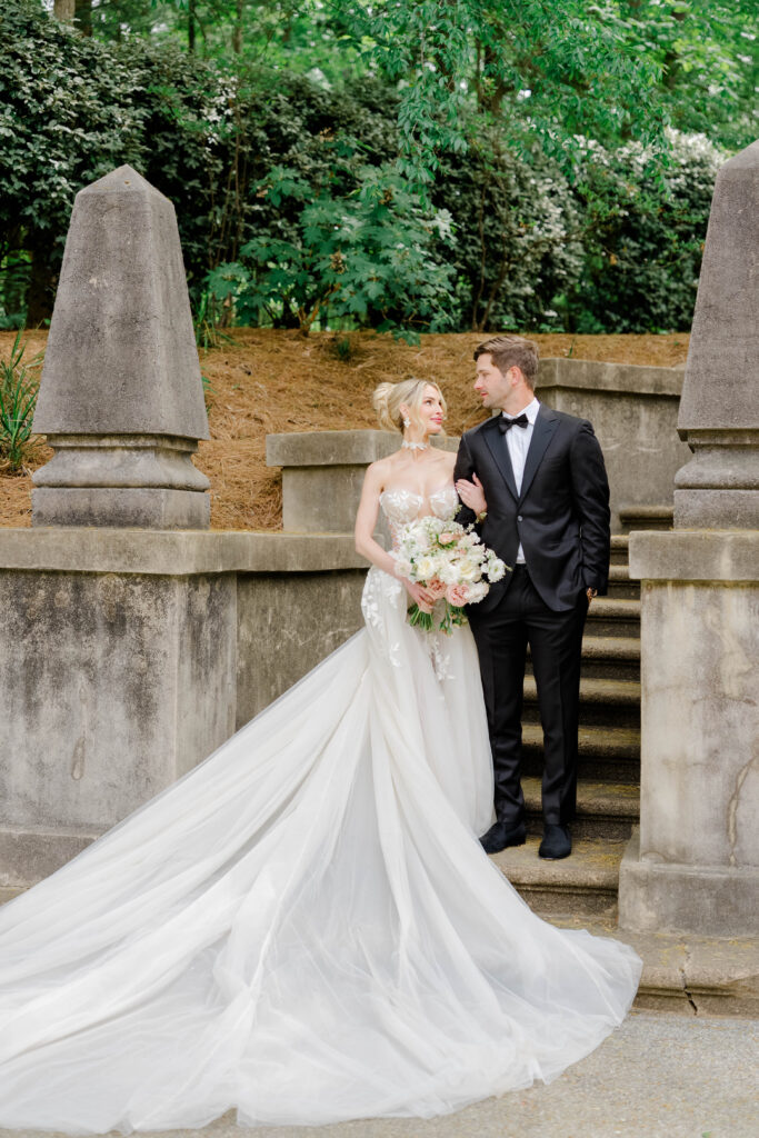 A bride and groom stand on the Swan House stone staircase, with the gown’s flowing train adding movement against the historic architecture. Elegant portrait inspiration from a Swan House wedding in Atlanta.