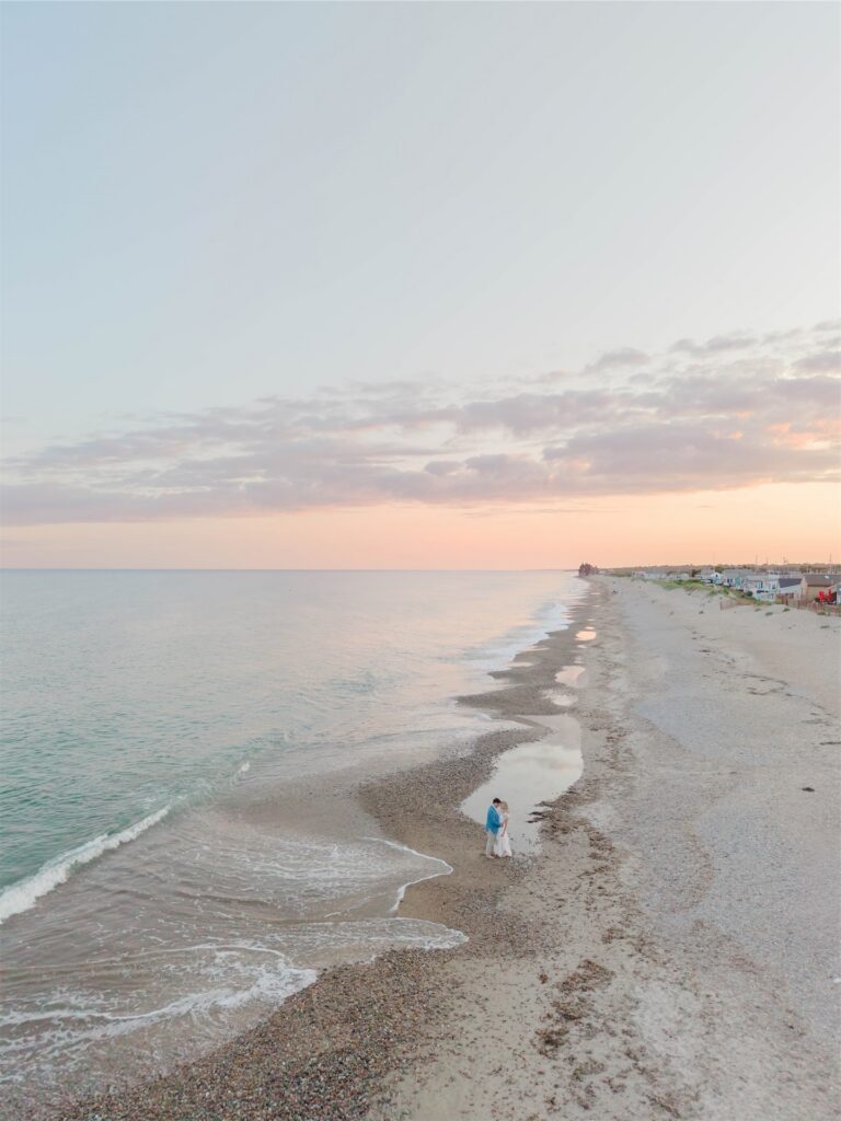 Aerial view of Molly and Anthony walking along a quiet Rhode Island shoreline during their beach engagement session.