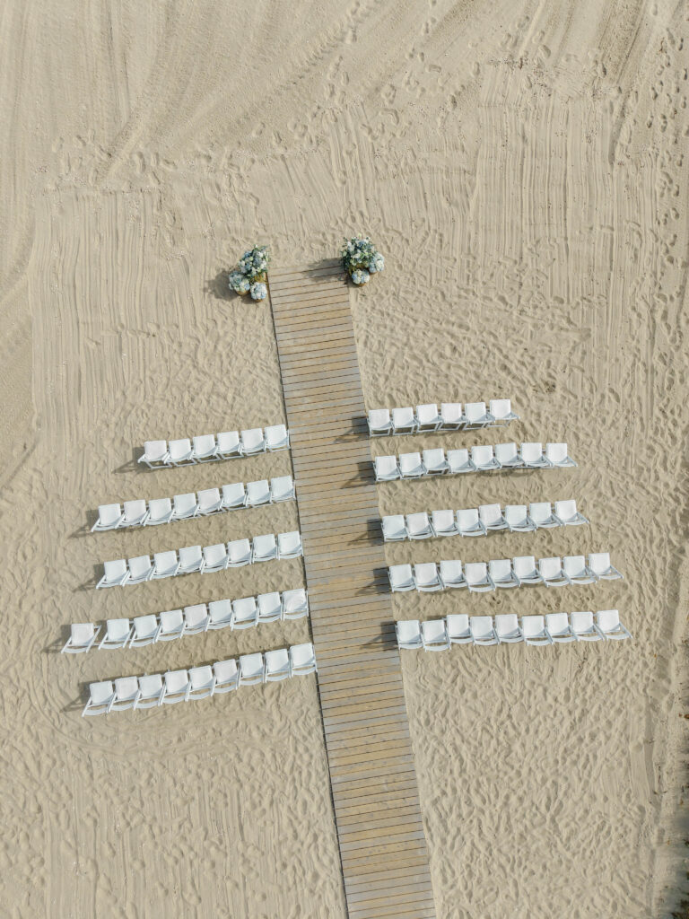 Wedding escort cards arranged along a wooden boardwalk in the sand for a Cape Cod wedding.
