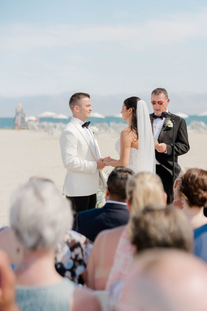 Bride and groom exchanging vows during an outdoor Cape Cod beach wedding ceremony with guests watching.